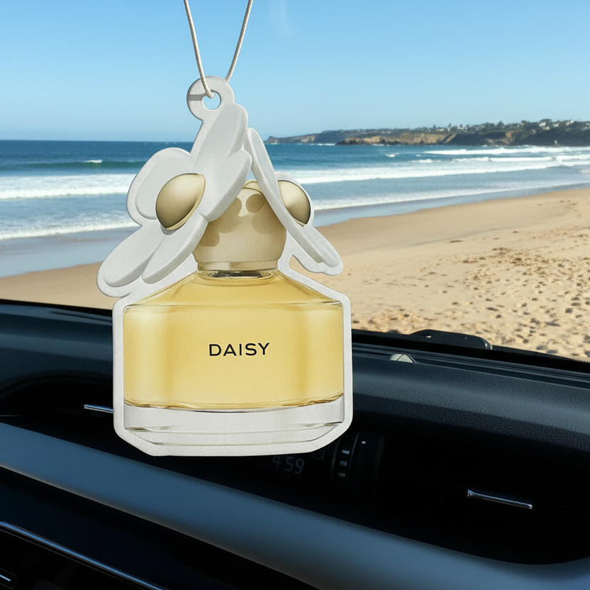 Car air freshener shaped like a perfume bottle with 'DAISY' branding on a car dashboard, beach in the background.