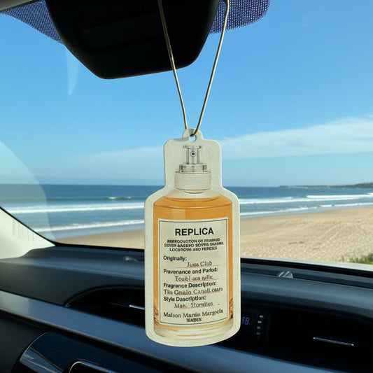 Car air freshener hanging from a car's rearview mirror with a scenic road view outside.