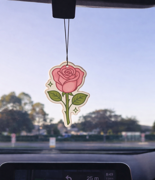 Car air freshener with a rose design hanging from a car's rearview mirror.